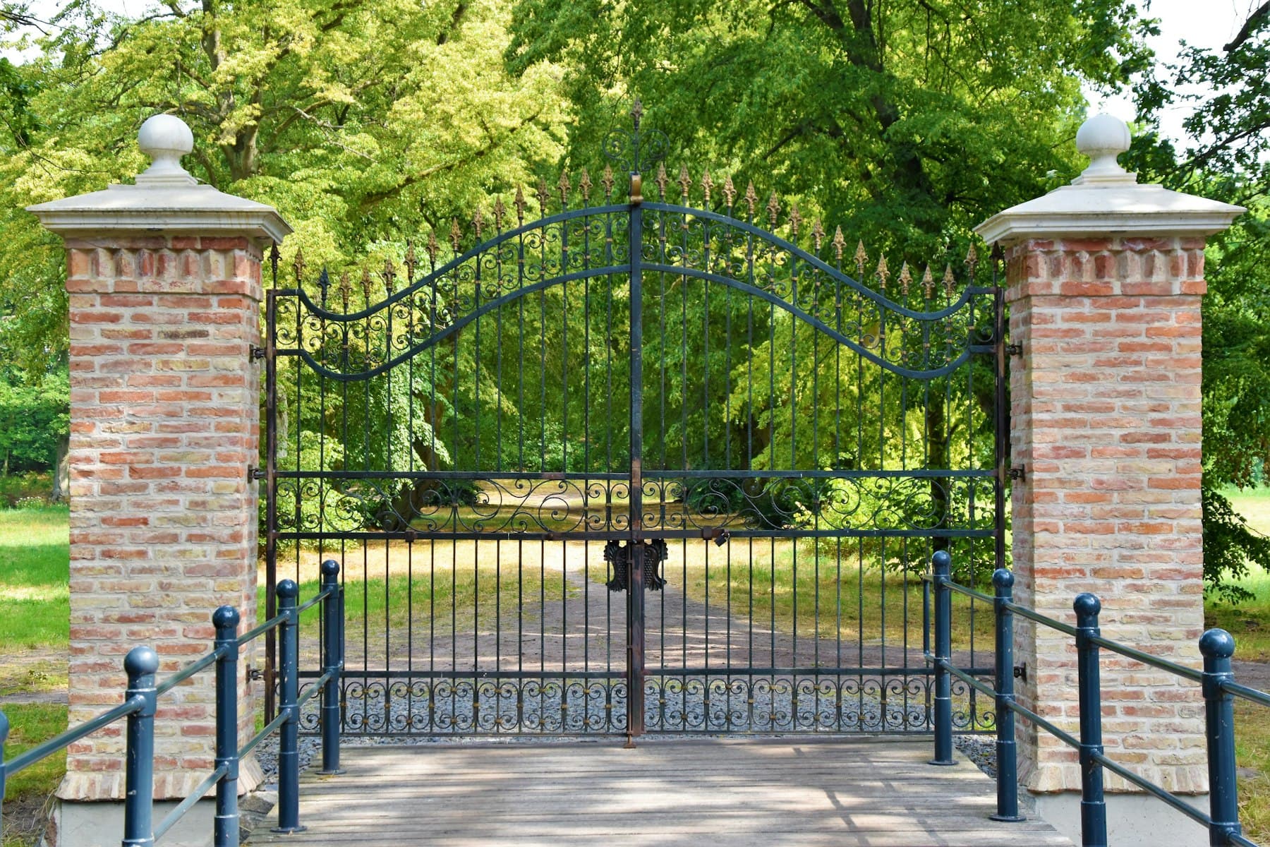 Black iron double swing gate between brick pillars
